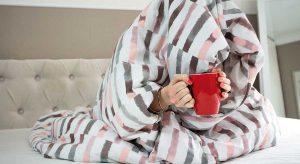 Frau trinkt Tee unter einer Bettdecke