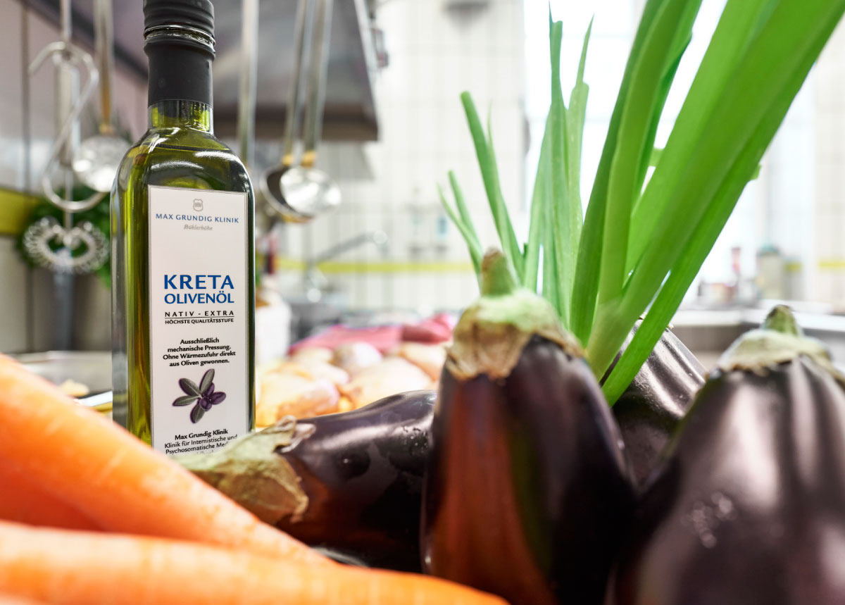 Flasche mit nativem Olivenöl und Gemüse im Hintergrund