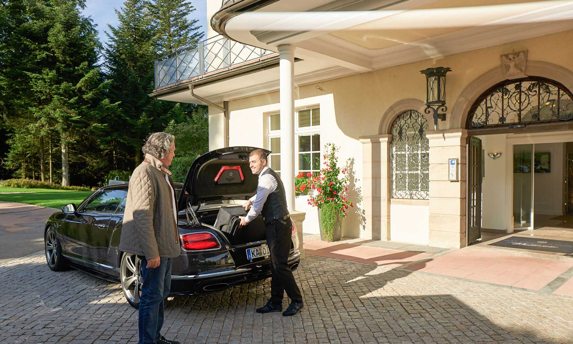 An- oder Abreise eines Gastes in der Max Grundig Klinik, Darstellung Serviceleistung am Auto mit Gast und Mitarbeiter, der Koffer einlädt